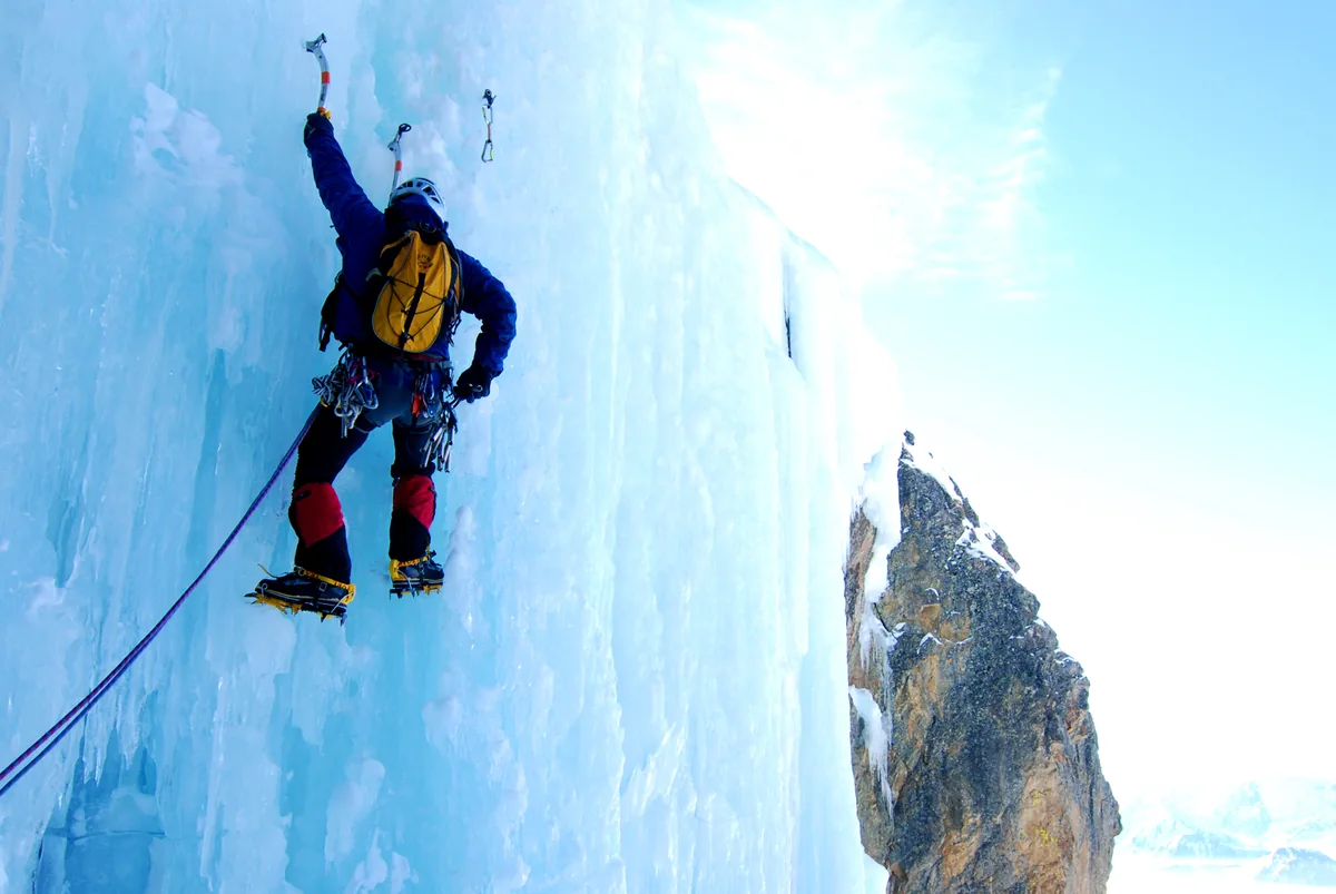 Grimpeur équipé de piolets et de crampons sur une cascade gelée