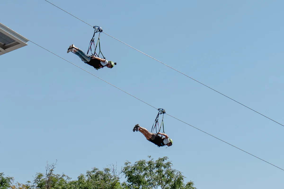 Deux personnes suspendues en position allongée sur une double tyrolienne