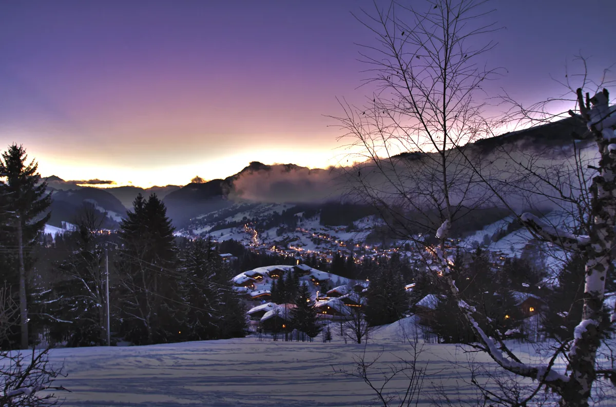 Village des Gets enneigé au crépuscule, au pied des montagnes.