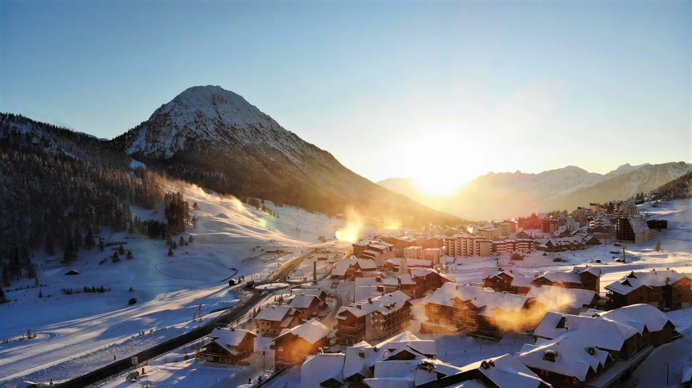 Bâtiments enneigés de Montgenèvre et montagnes sous une lumière dorée.