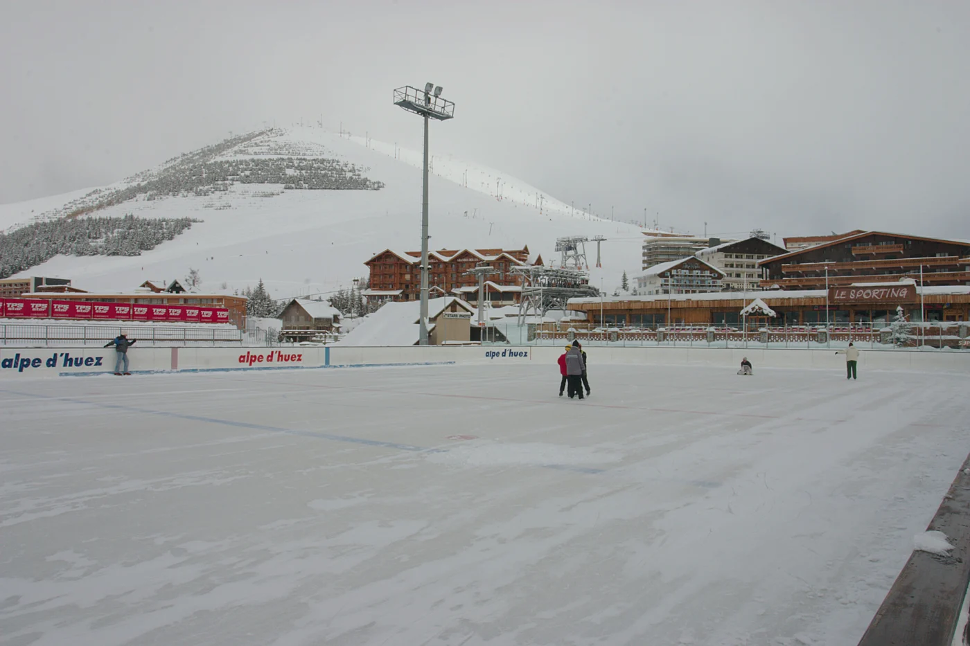 Patinoire extérieure de l’Alpe d’Huez devant les bâtiments de la station et les montagnes enneigées.