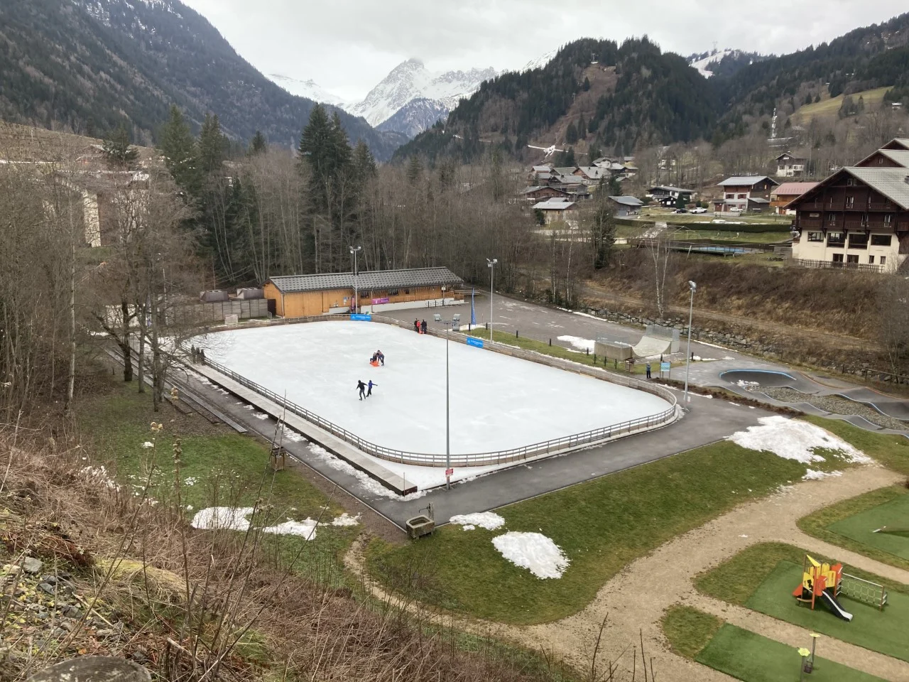 Patinoire extérieure des Contamines-Montjoie, village et montagnes en arrière-plan.