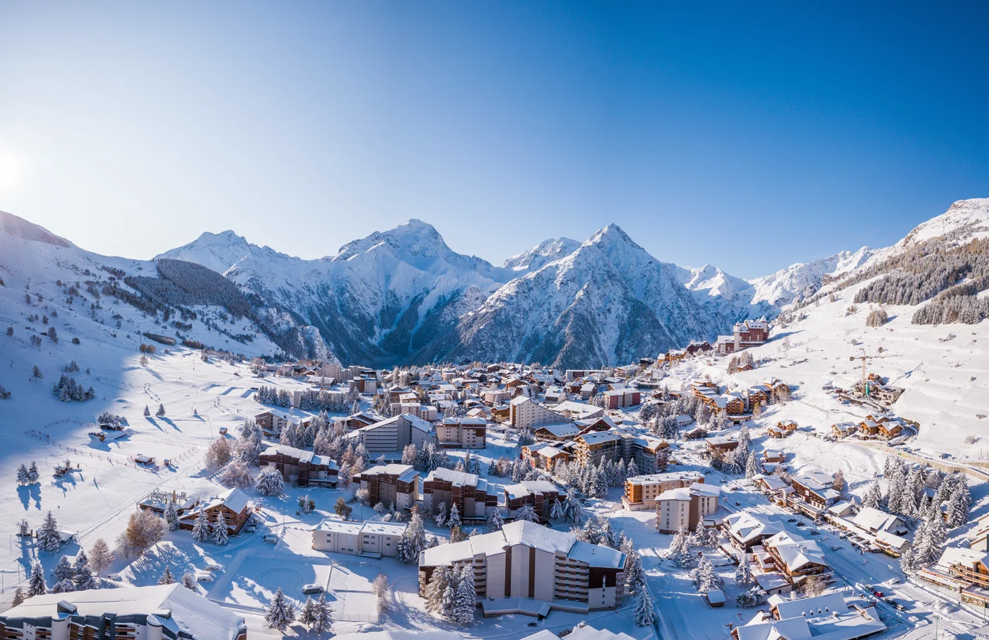 Bâtiments des Deux Alpes sous la neige, au pied de montagnes enneigées.