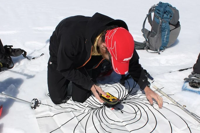 Un participant manipule un DVA au-dessus d’un support pédagogique posé sur la neige, en Suisse.
