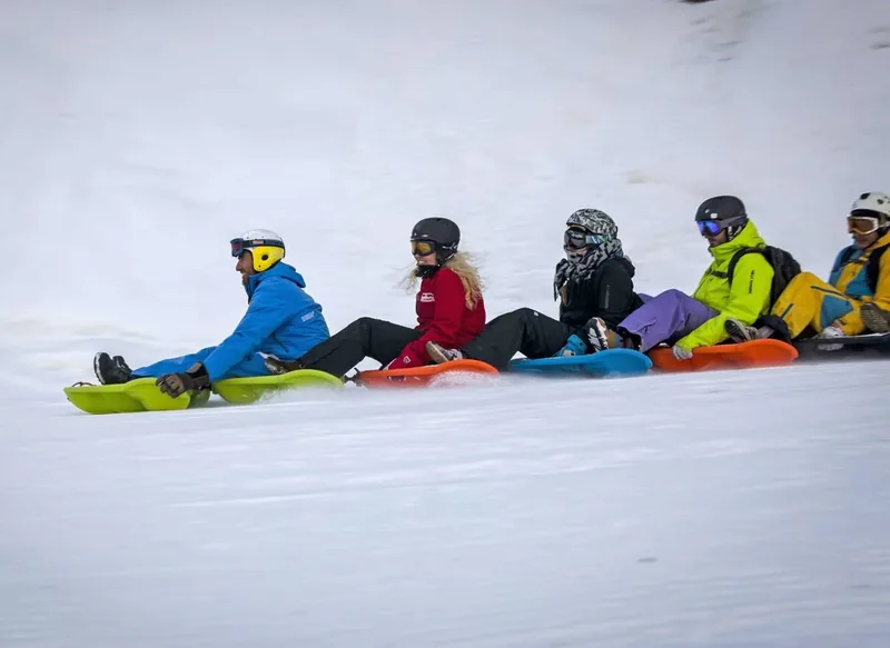 Groupe assis sur des luges articulées pendant une descente de Snakegliss aux Contamines-Montjoie.